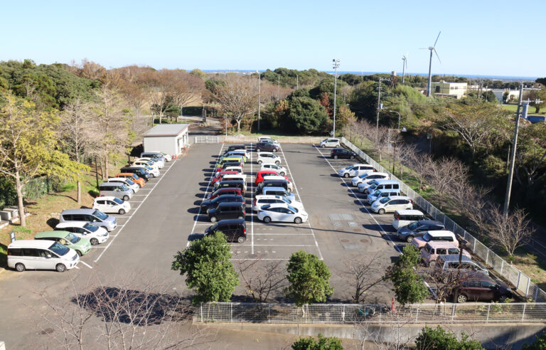 介護施設の駐車場と周辺環境。多数の車が停めてあり、緑に囲まれた立地。