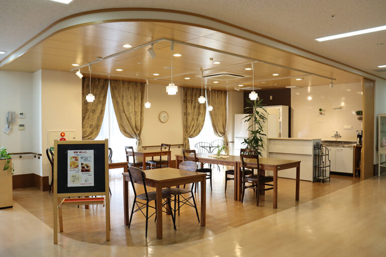 介護施設の食堂・ダイニングエリア。木製テーブルと椅子が配置され、明るく清潔な空間。
